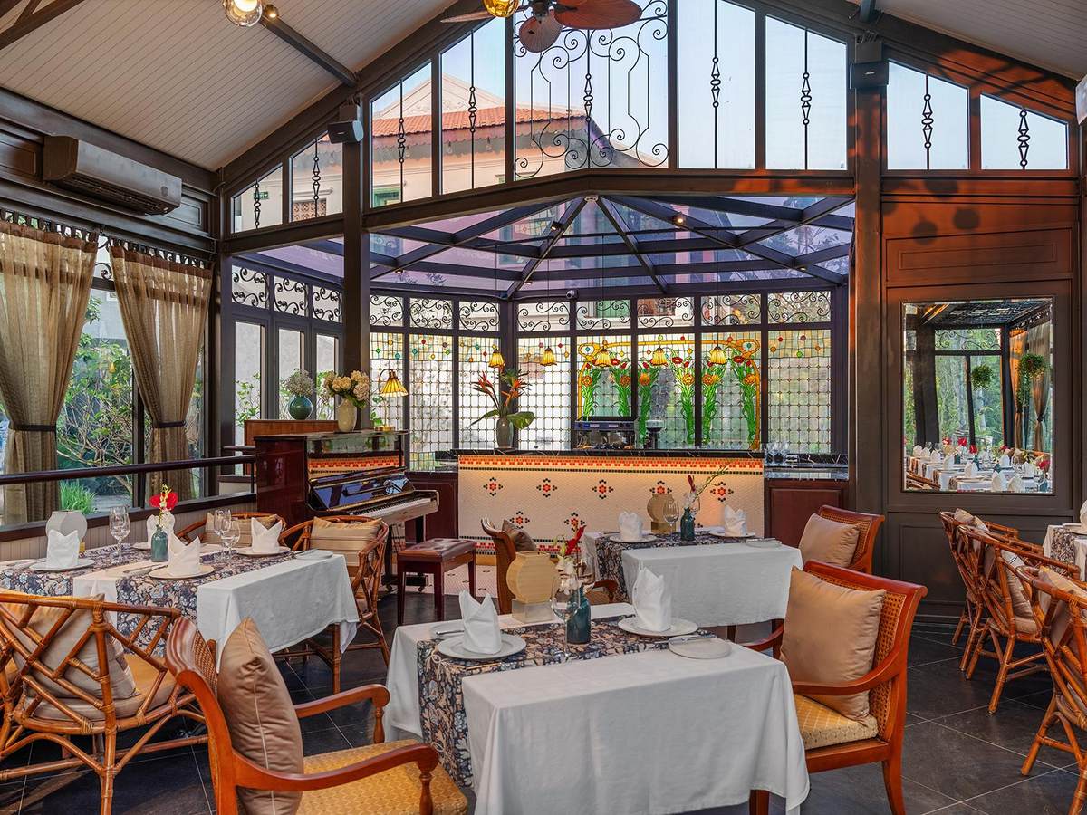 Glasshouse restaurant with black iron window frames, rattan armchairs, blue-and-white table runners and greenery outside