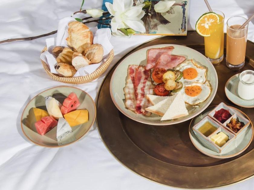 Breakfast on white bedding: a brass tray with eggs, bacon and toast, a basket of pastries, sliced fruit, orange juice and white flowers