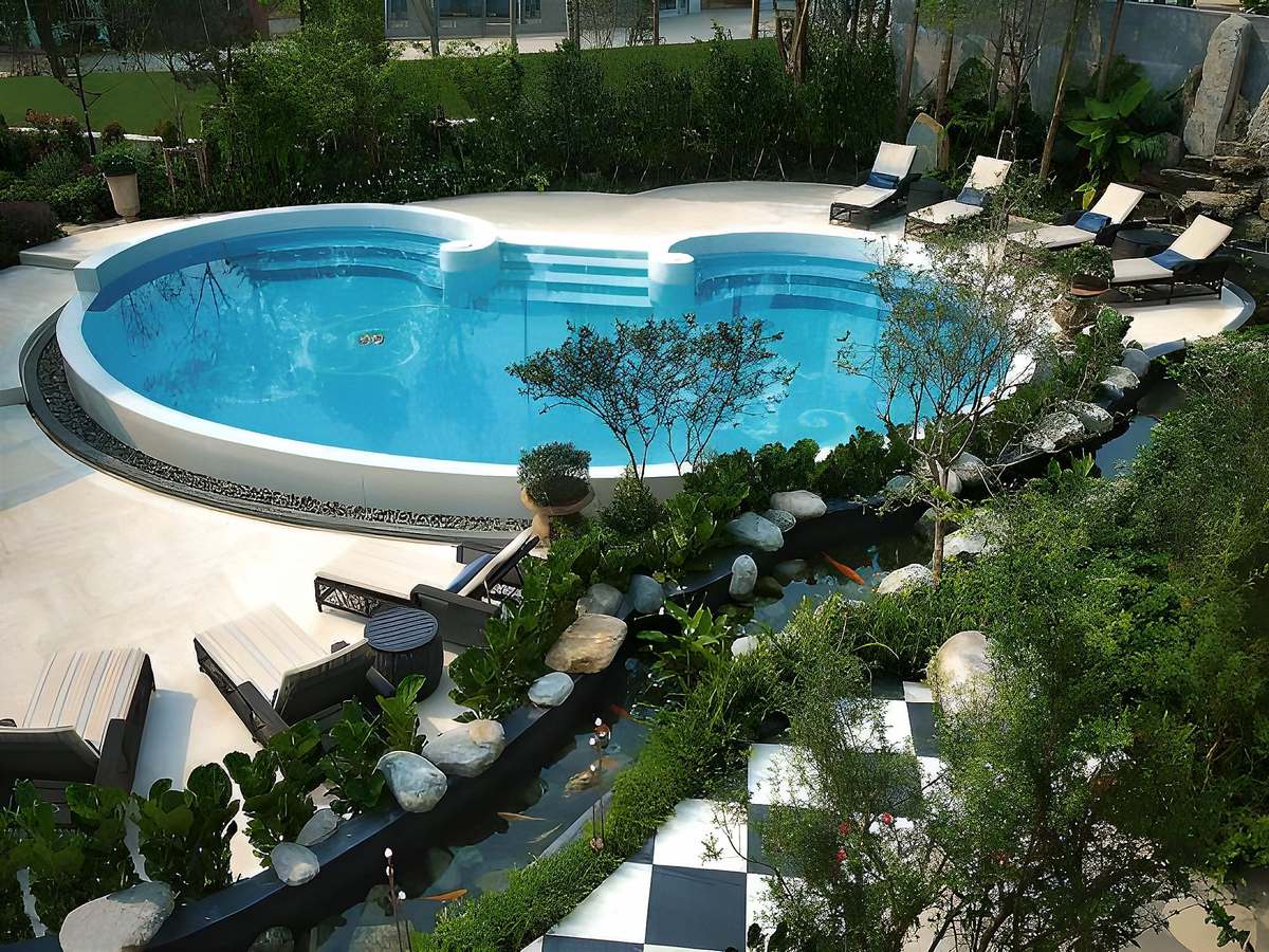 Curving pool with a round section, white sandstone deck and loungers seen from above beside a terrace with a checkerboard floor