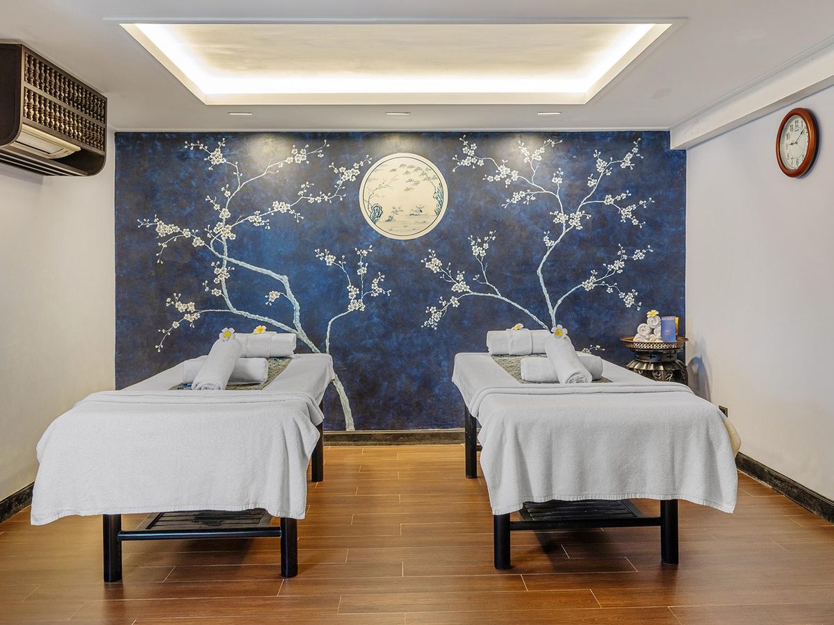 Spa treatment room with two massage beds, folded white towels and dark blue wallpaper with a pattern of white birds and branches