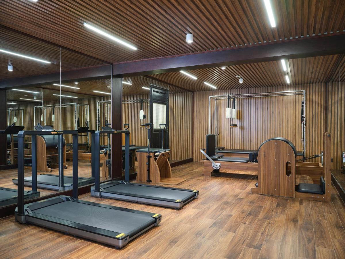 Small gym with treadmills and a reformer machine on a wooden floor behind glass walls with a slatted wooden ceiling