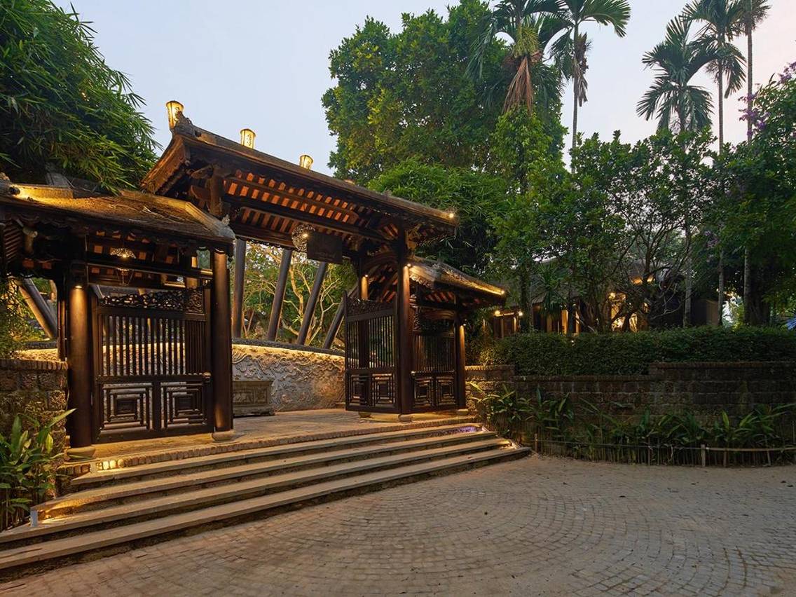 Wooden gate with a curved tiled roof and stone steps under tall trees at the entrance to the garden houses