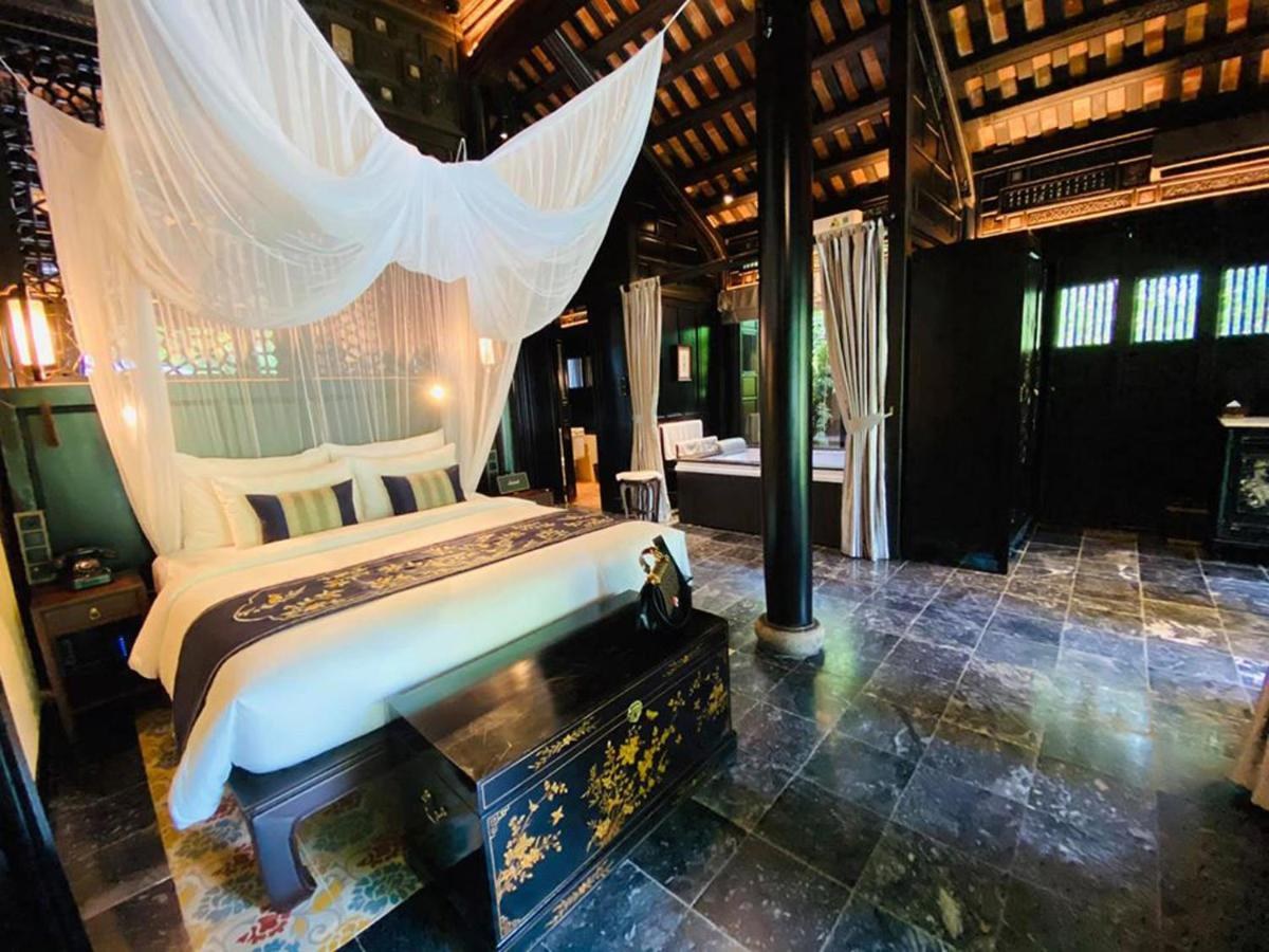 Garden-house bedroom with a bed under a white mosquito-net canopy, a dark lacquered chest, stone floor and tall wooden columns