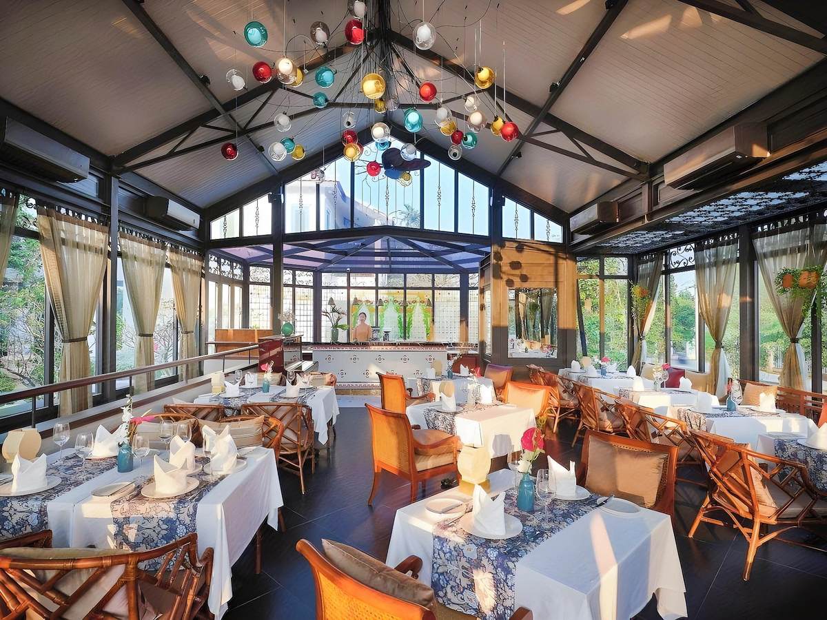 Glasshouse restaurant with a peaked glass roof, coloured hanging lanterns, rattan chairs and tables set with white cloths