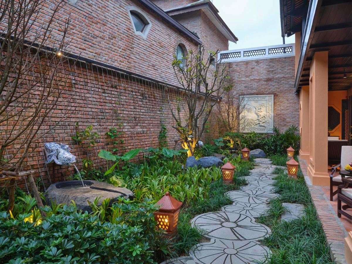 Narrow garden path of stepping stones between a brick wall and the side of a house, with lanterns and plants along the way