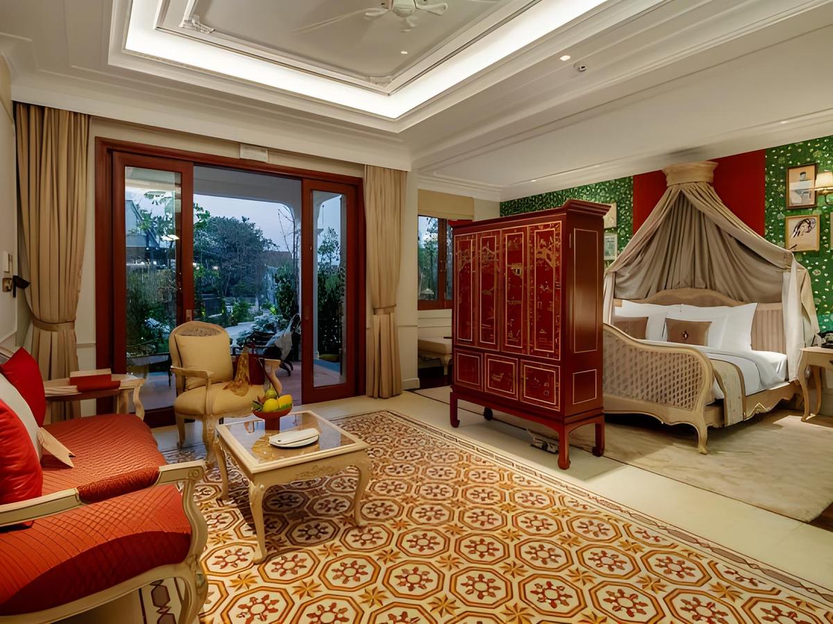 Villa suite with a canopied rattan bed, green botanical wallpaper, a red lacquer cabinet and windows onto garden trees