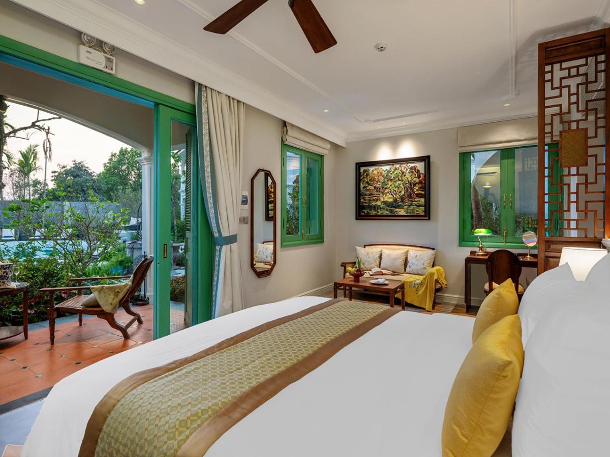 Bright villa bedroom with a king bed, gold cushions, a ceiling fan and green-framed glass doors to a balcony