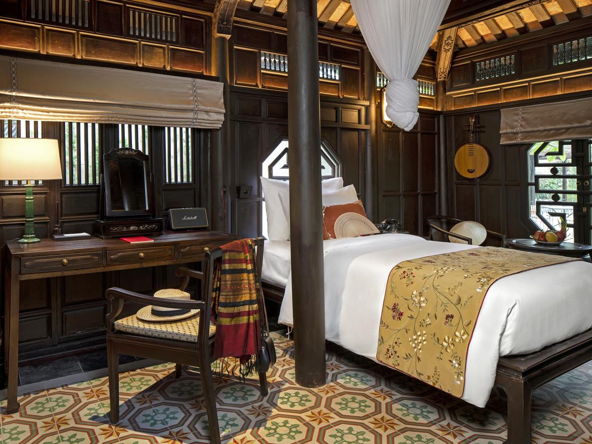 Garden-house bedroom with dark wooden walls, a bed with a gold embroidered runner, a writing desk and an octagonal lattice window