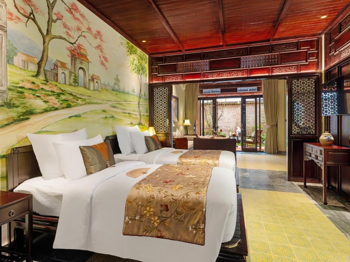 Twin room under a high wooden roof with two white beds, gold runners and a painted village mural on the wall