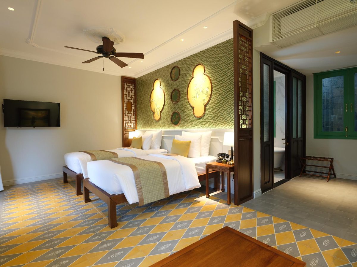 Villa twin room with two beds, gold and green headboard panels, a ceiling fan and a yellow patterned tiled floor