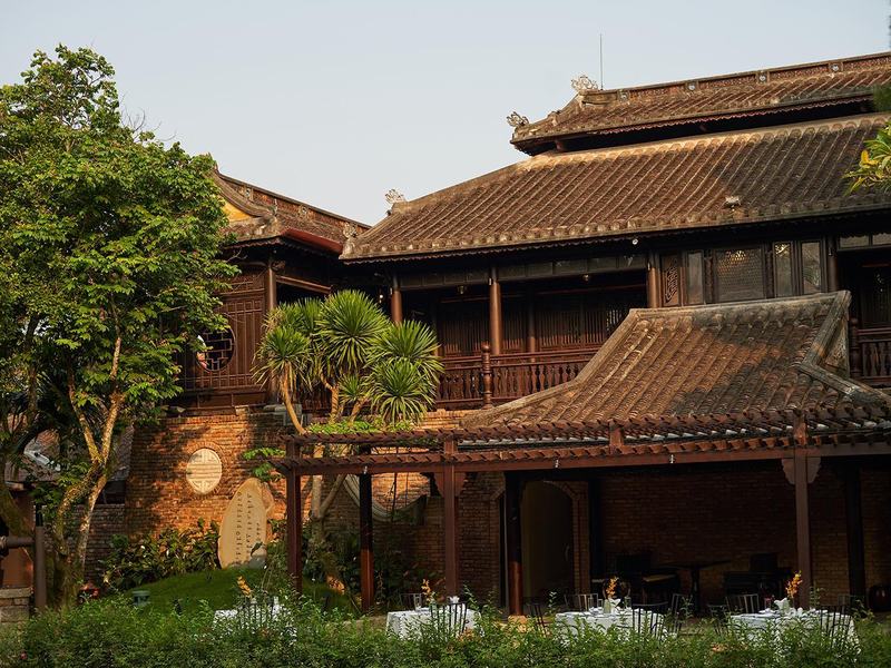 Two-storey dark-wood garden house with layered tiled roofs, a brick lower wall with round medallions and garden tables in front