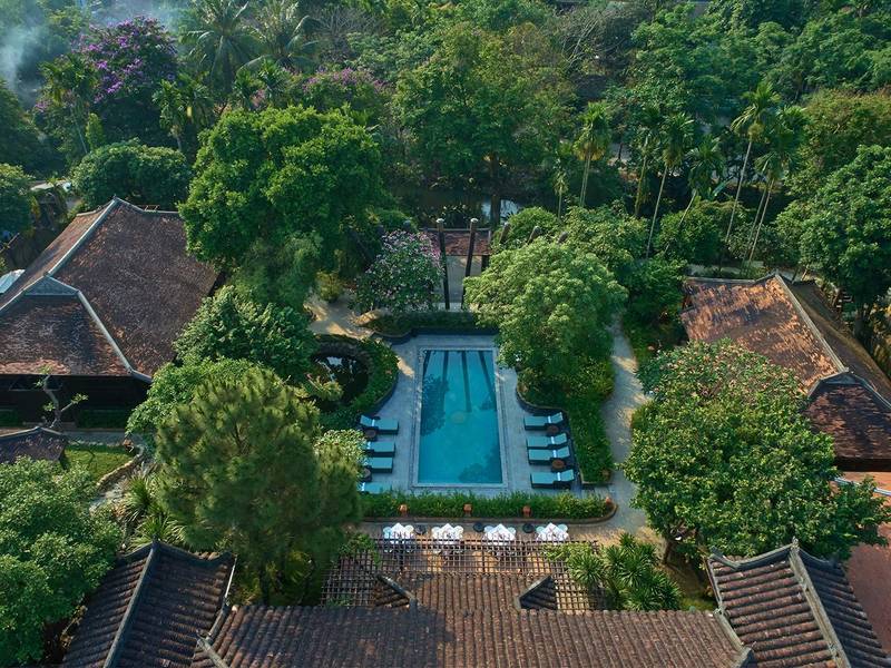 Aerial view of a long rectangular pool between tall trees and old tiled roofs