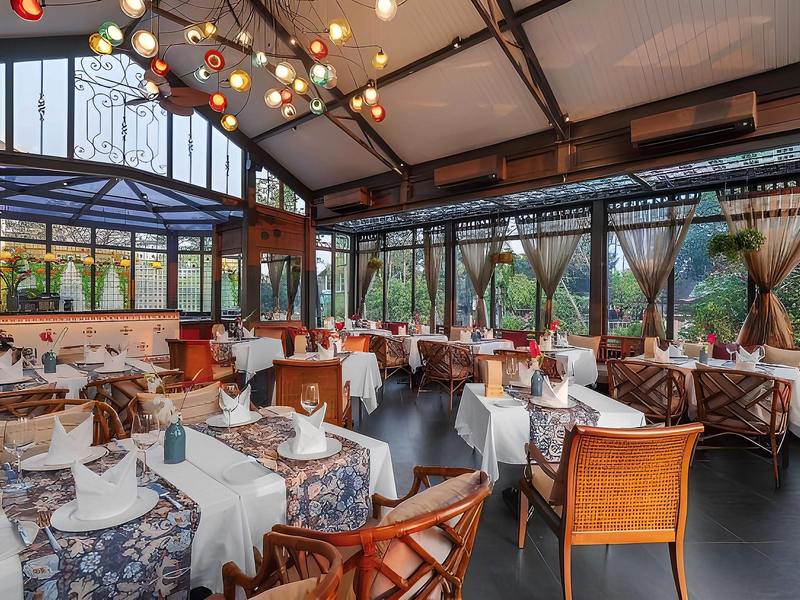 Glasshouse dining room with a black iron frame, coloured glass lanterns, rattan chairs and white tablecloths